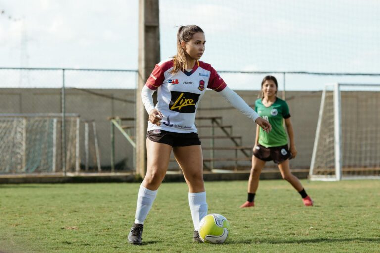 Two teenage girls engaged in a soccer game on an outdoor field, wearing sportswear.