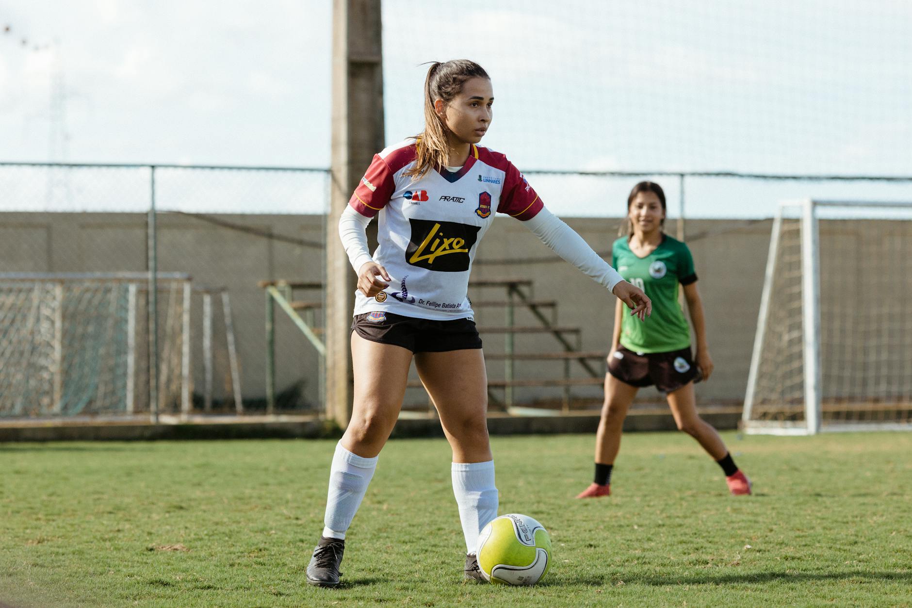 Two teenage girls engaged in a soccer game on an outdoor field, wearing sportswear.