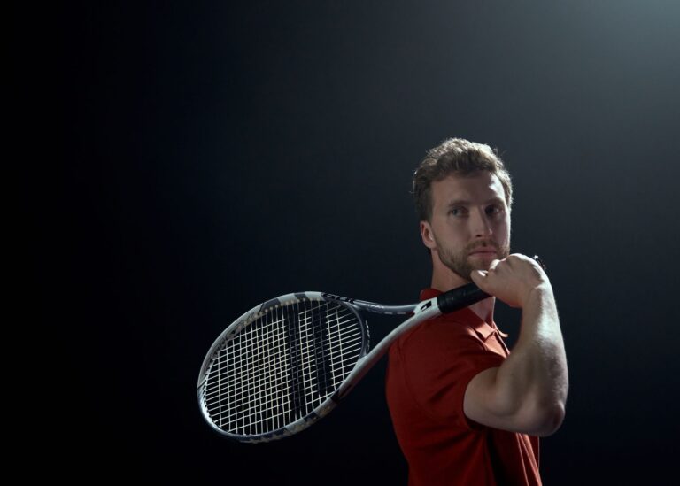 A focused tennis player holding a racket, preparing for a shot against a dark background.