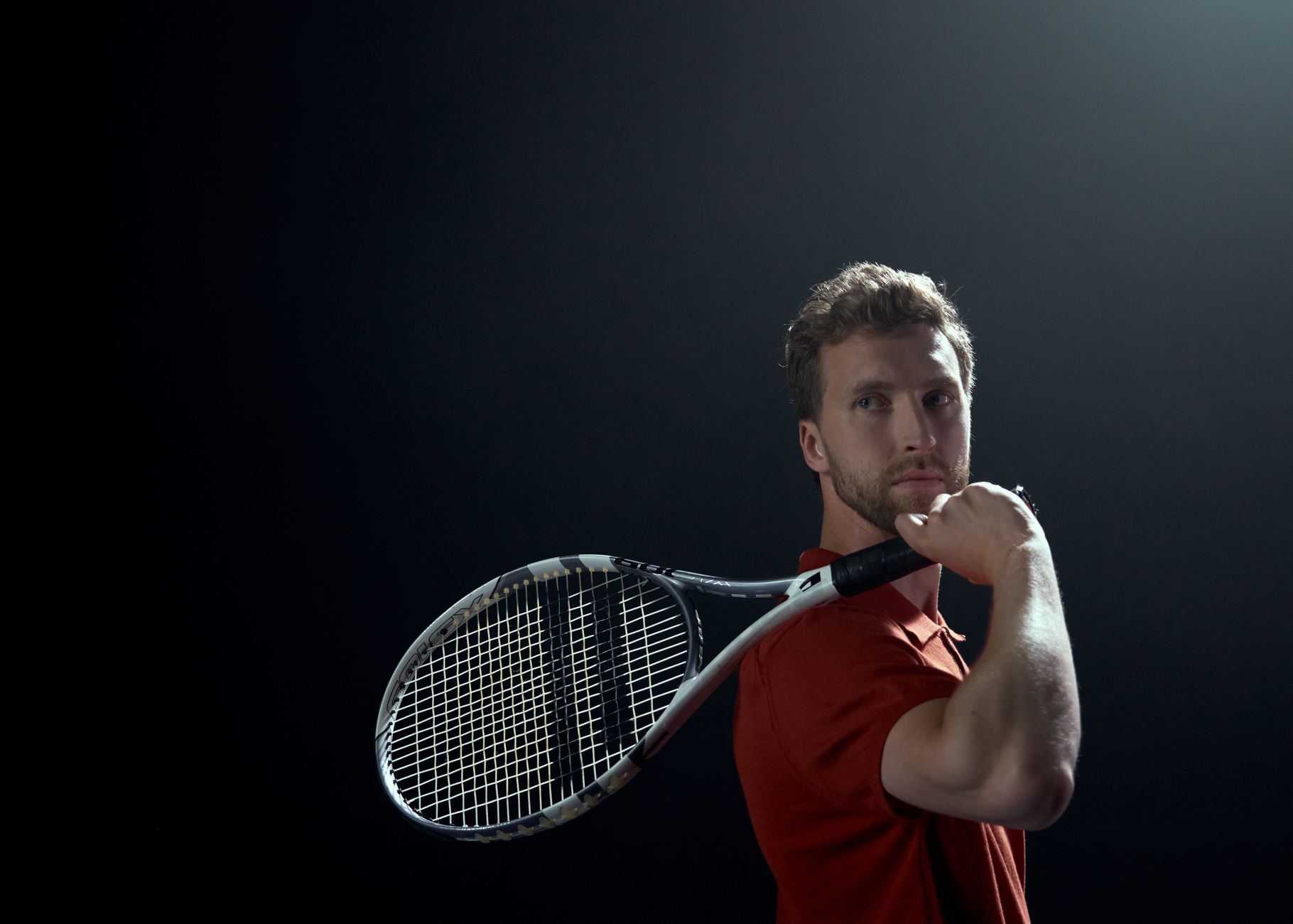 A focused tennis player holding a racket, preparing for a shot against a dark background.