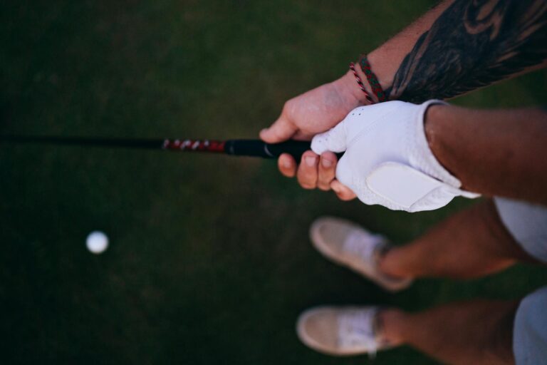 Close-up of a golfer's hands with a tattoo and glove, holding a golf club on a grassy field.