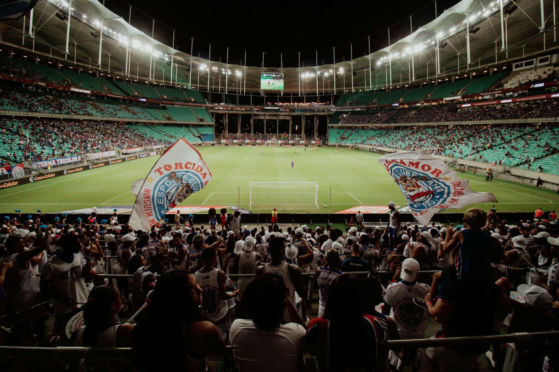 Energetic soccer fans cheer during a night match at a large stadium, creating an exciting atmosphere.
