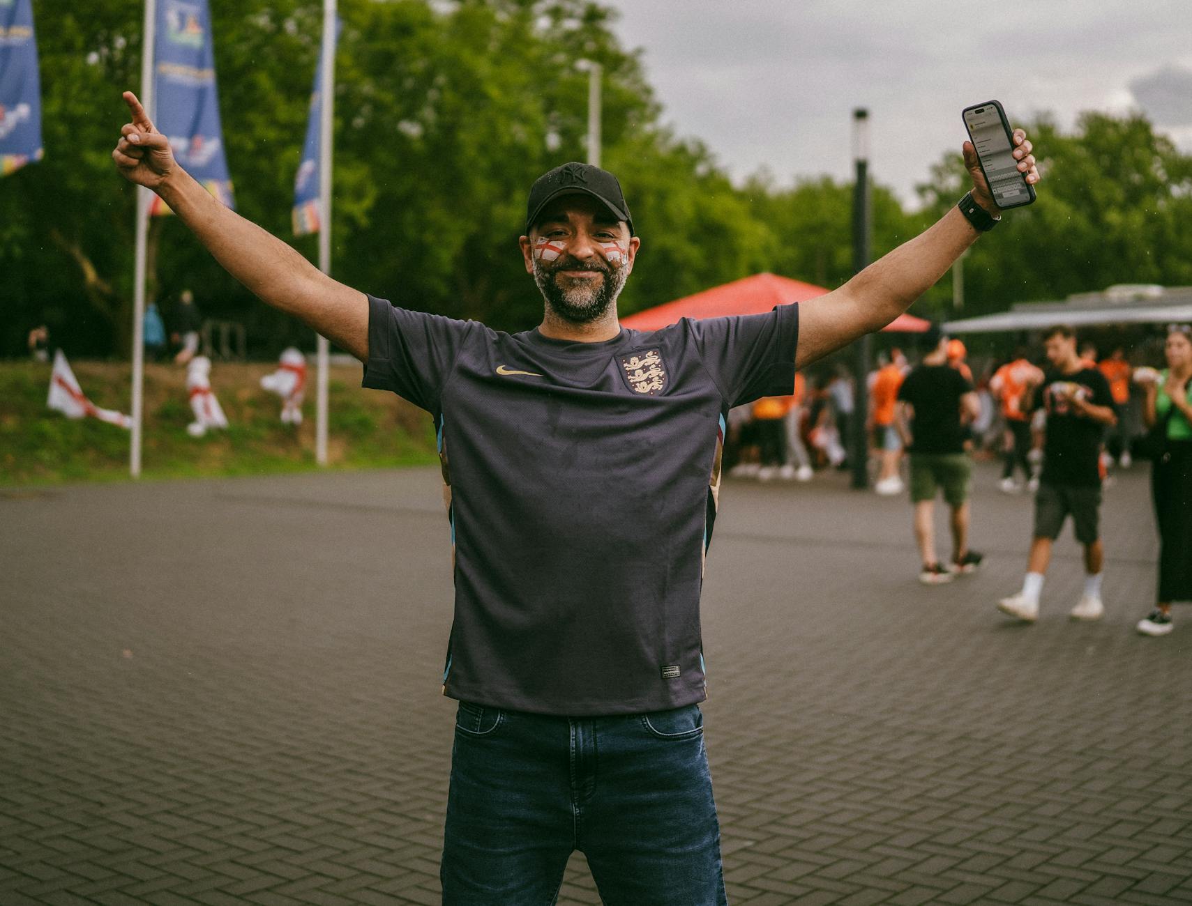 Joyful soccer fan with arms raised, celebrating outdoors in casual sportswear.