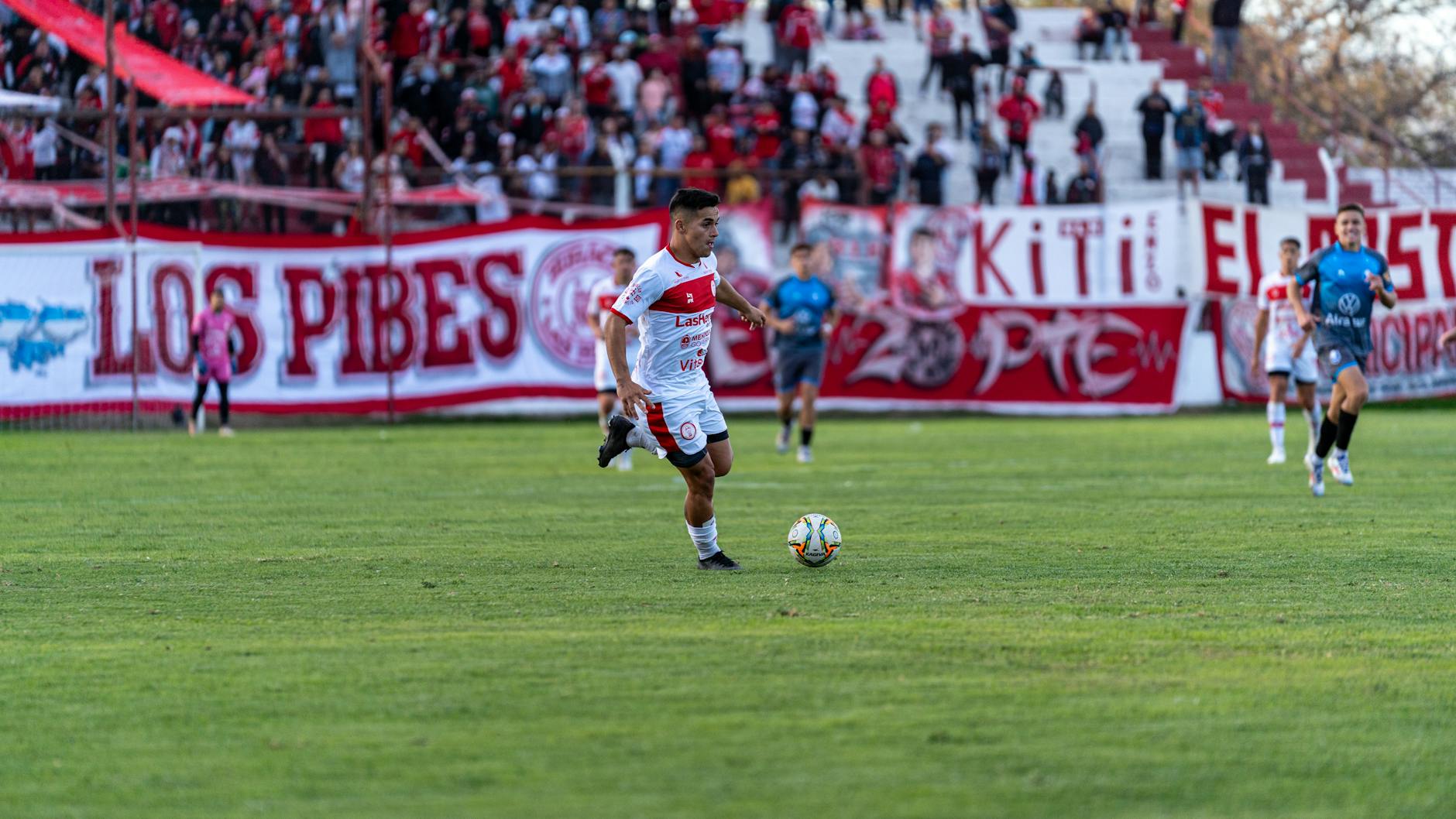 Action shot of a football match with players and vibrant fan presence in the stadium.