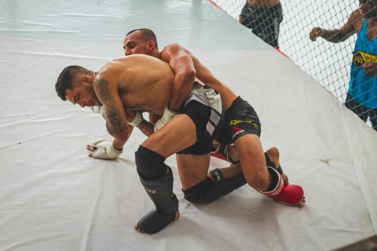 Two male athletes engage in intense grappling during MMA training session indoors.