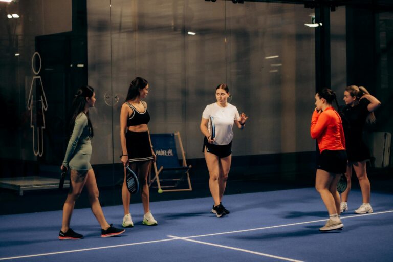Group of women playing paddle tennis indoors, discussing strategies in an evening match.