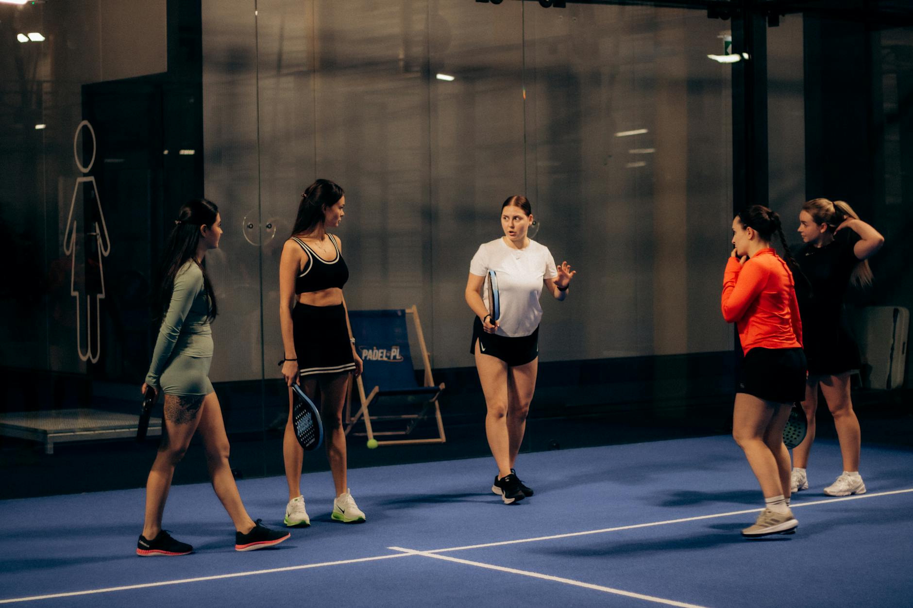 Group of women playing paddle tennis indoors, discussing strategies in an evening match.