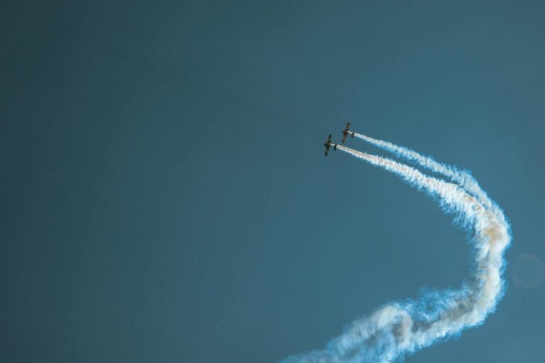 Two stunt planes performing in blue skies with artistic smoke trails.