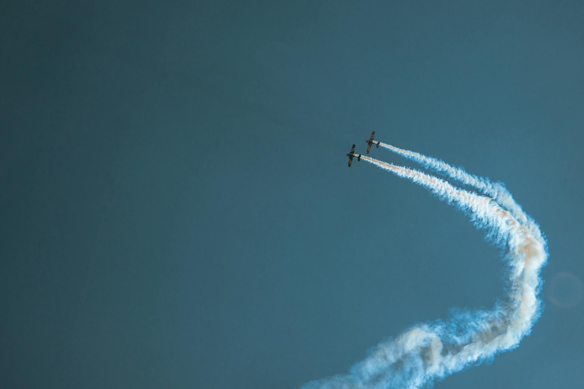 Two stunt planes performing in blue skies with artistic smoke trails.