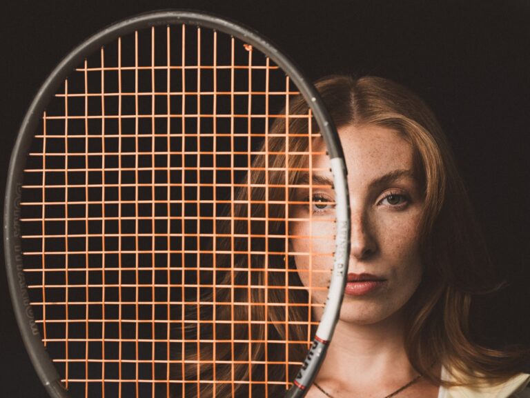 Professional portrait of a woman partially obscured by a tennis racket.