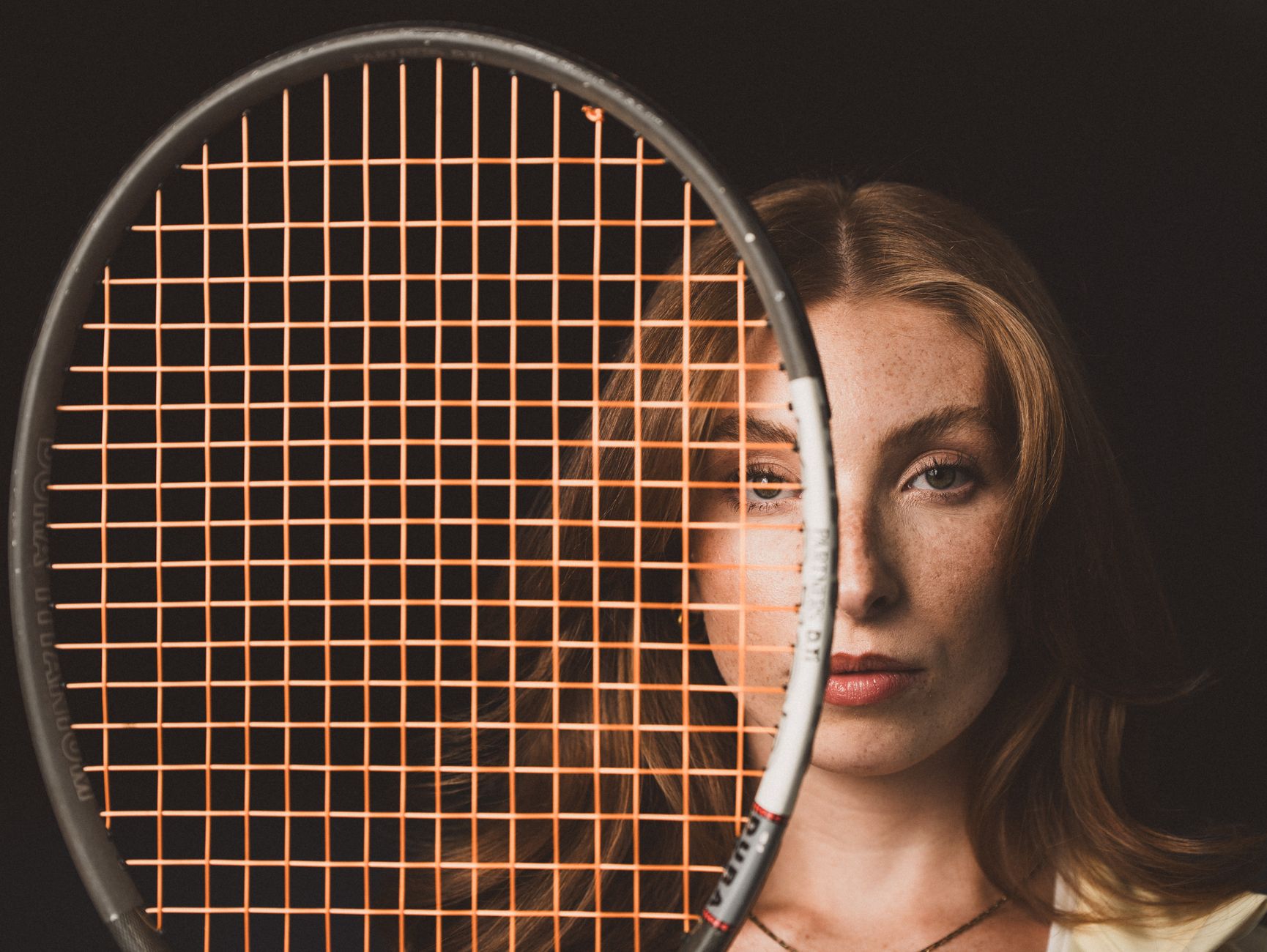 Professional portrait of a woman partially obscured by a tennis racket.