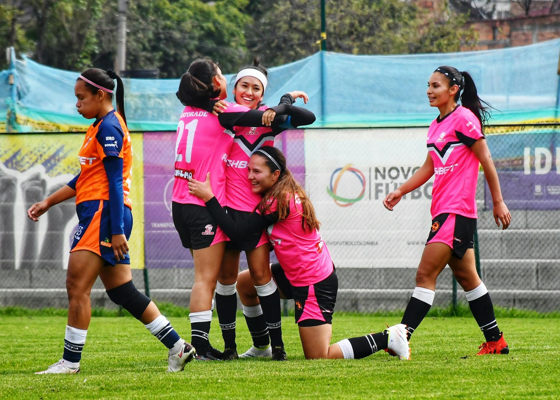 A women's football team celebrating victory on the field with embraces and smiles.