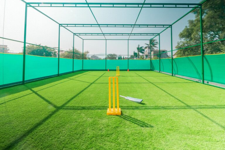 A cricket practice net with bright yellow stumps on a sunny day, ideal for training.