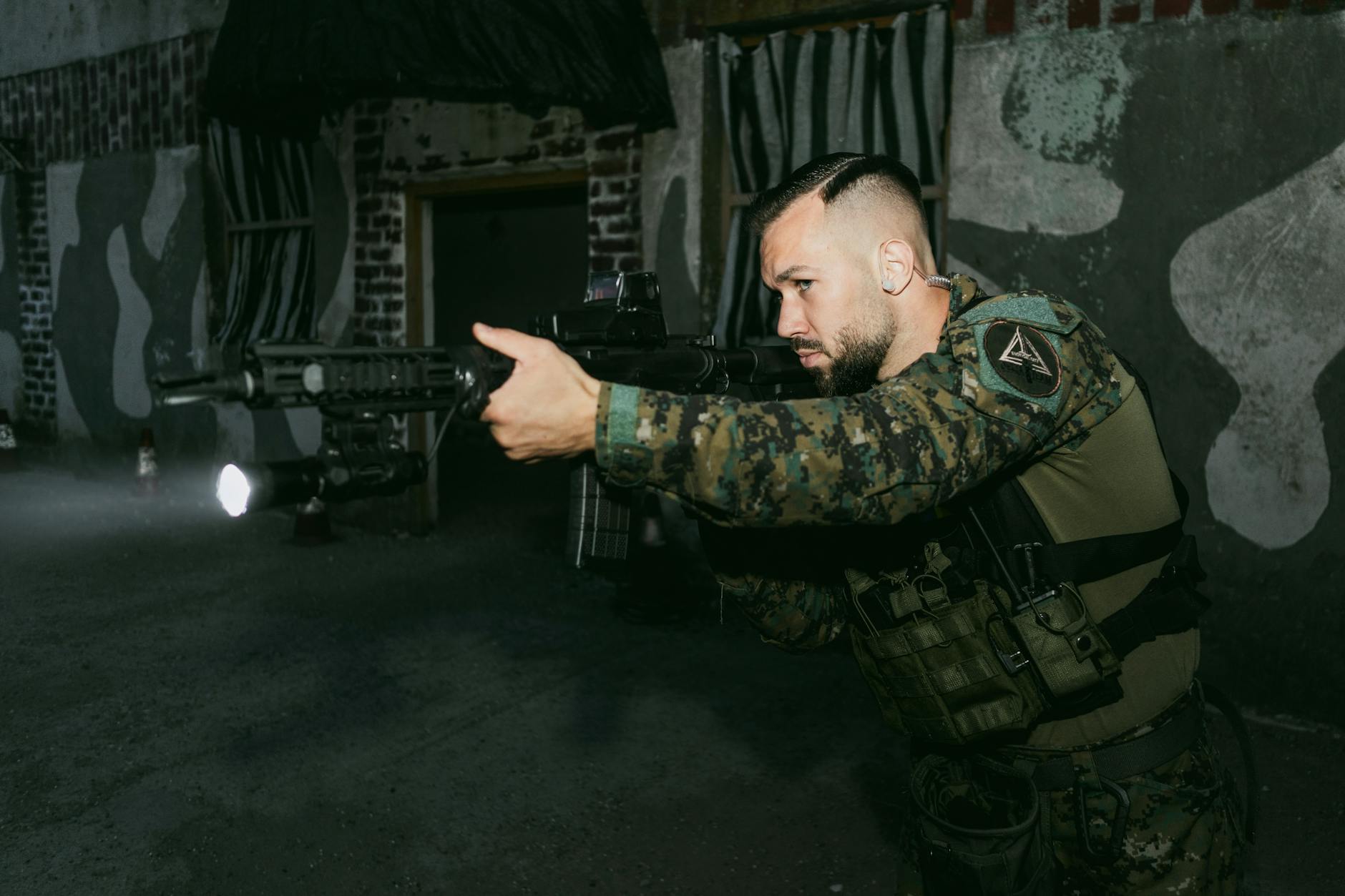 Focused soldier aiming rifle during training indoors at shooting range.