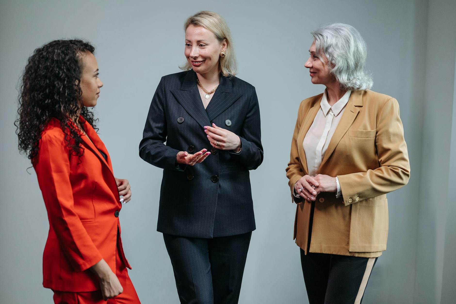 Three women in business attire having a conversation indoors, showcasing diversity and teamwork.