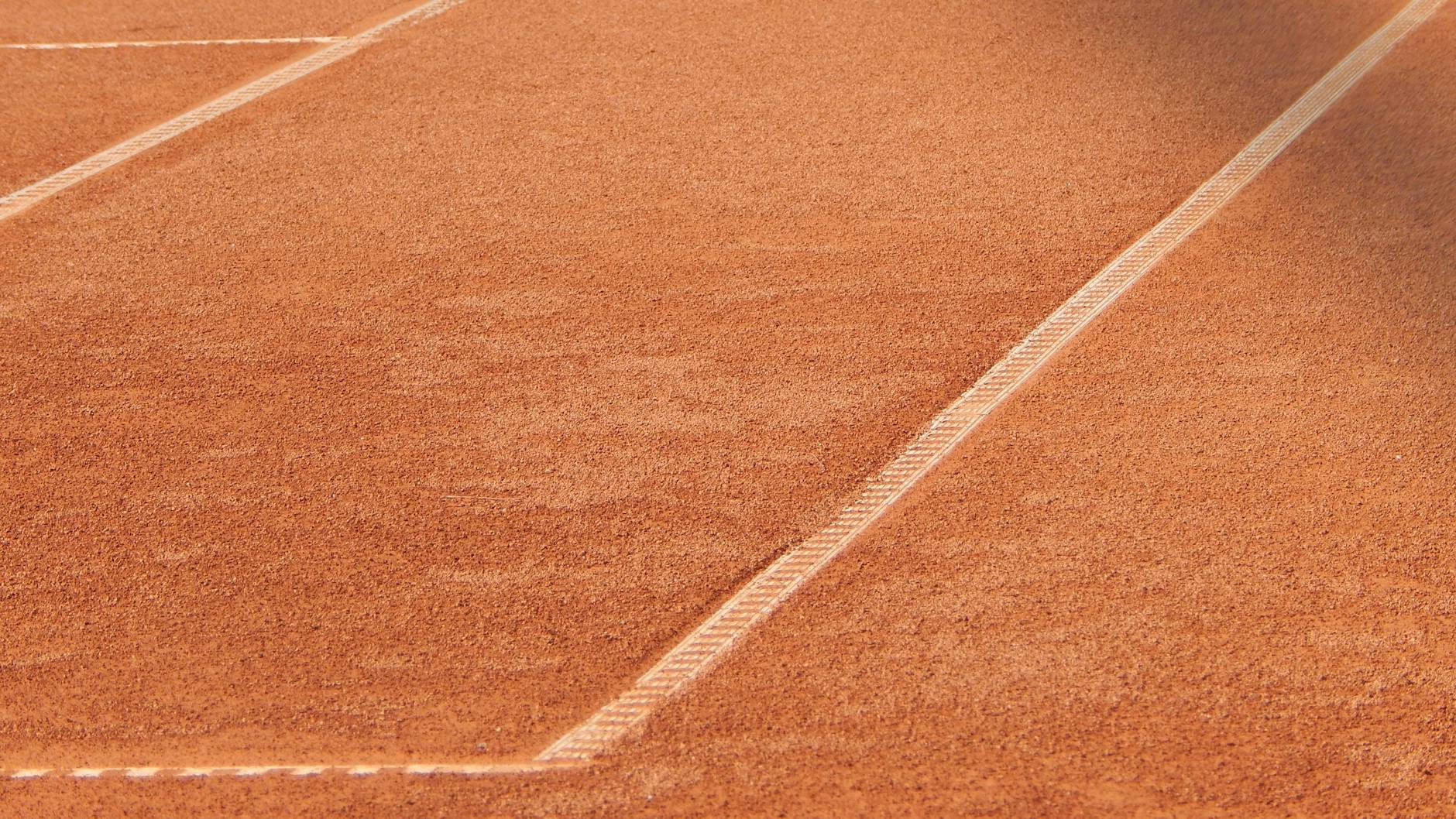 Close-up of a clay tennis court highlighting the detailed white line pattern.