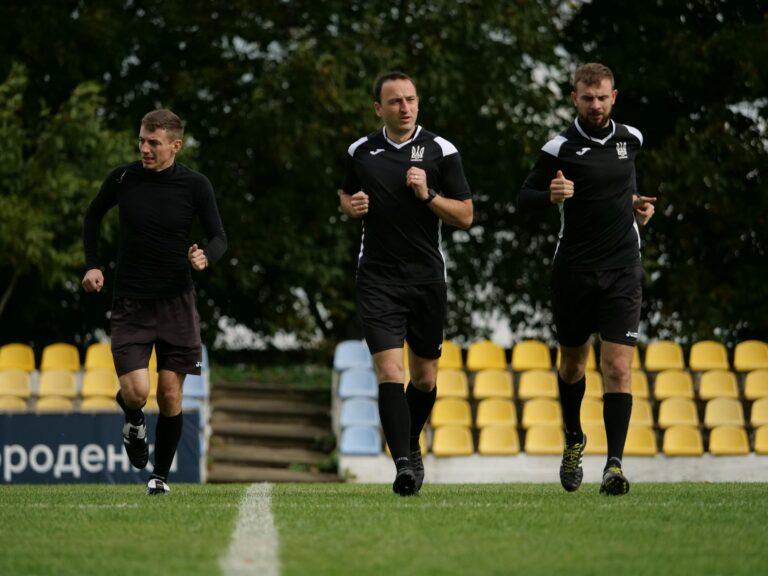 Three male referees running during a training session on a soccer field outdoors.