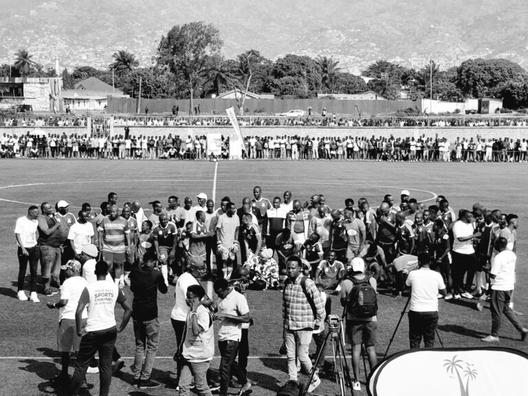 A diverse crowd gathers on a soccer field celebrating an event with vibrant community spirit.