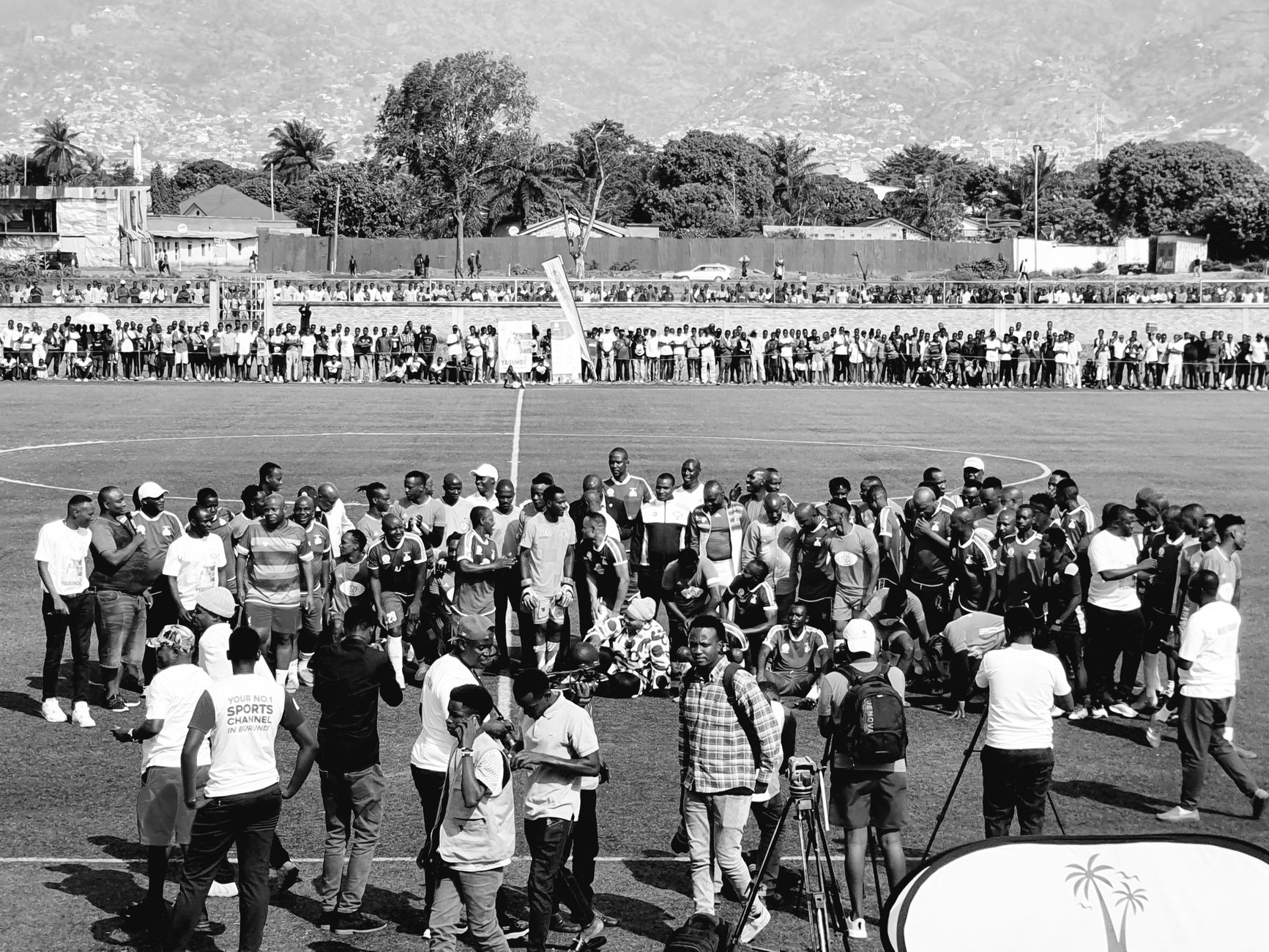 A diverse crowd gathers on a soccer field celebrating an event with vibrant community spirit.