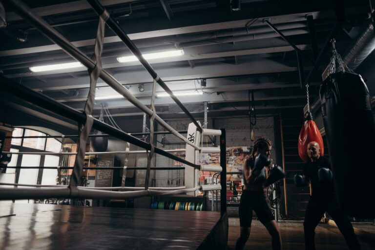 Two boxers training in a dimly lit gym with punching bags and equipment.