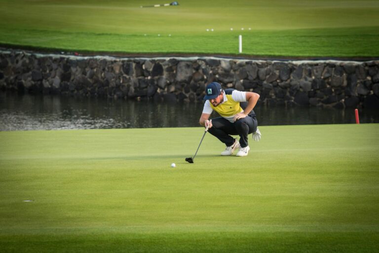 Golfer crouches to line up a putt on a sunny golf course morning.