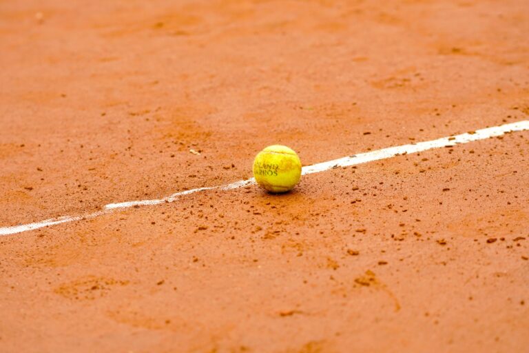 Tennis ball resting on a clay court, marked by a white line, ideal for sports themes.
