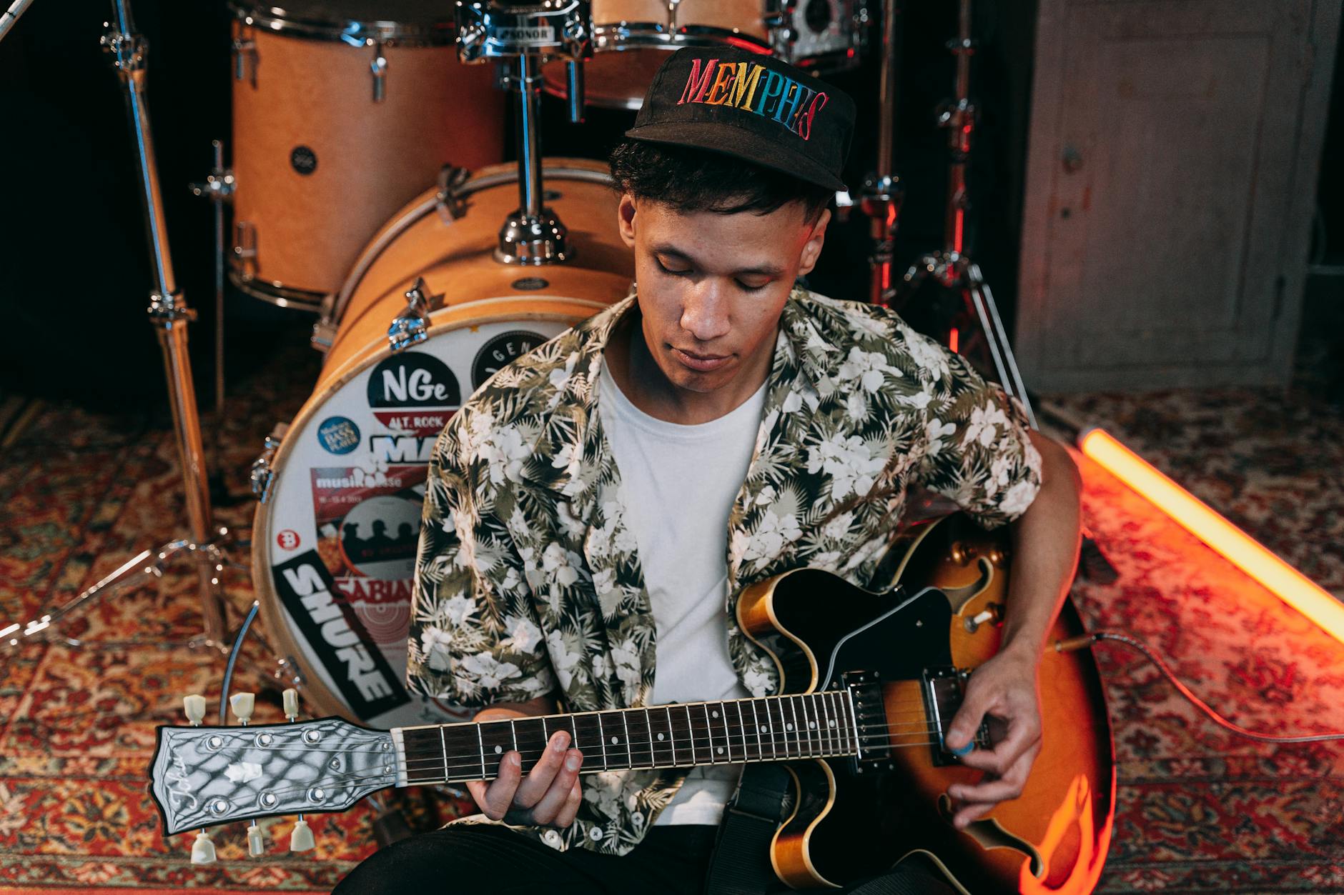 Asian male guitarist playing an electric guitar in a music studio setting.