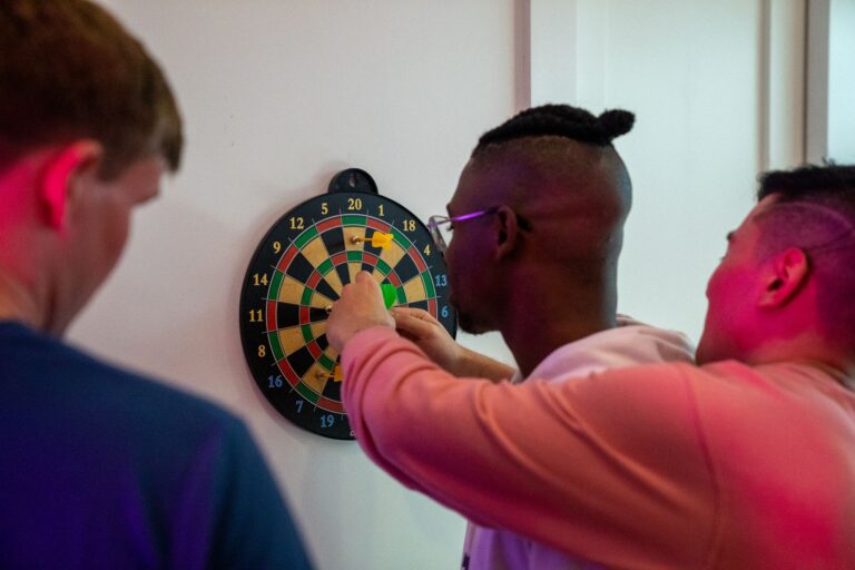 A group of adult friends enjoying a game of darts indoors, focusing on the dartboard.