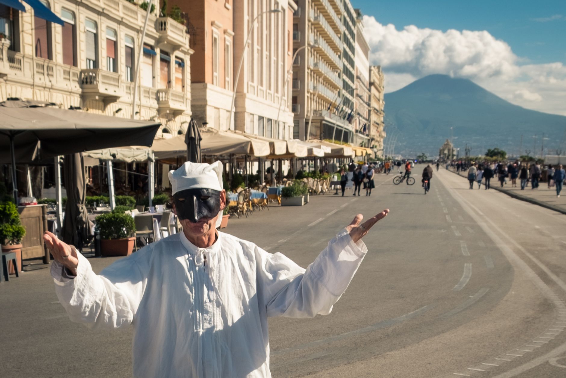 Pulcinella performer entertains on a bustling street in Naples, with Mount Vesuvius in the background.