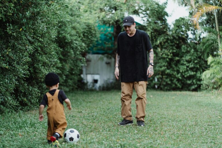A father and young son enjoying soccer together on a lush garden lawn.