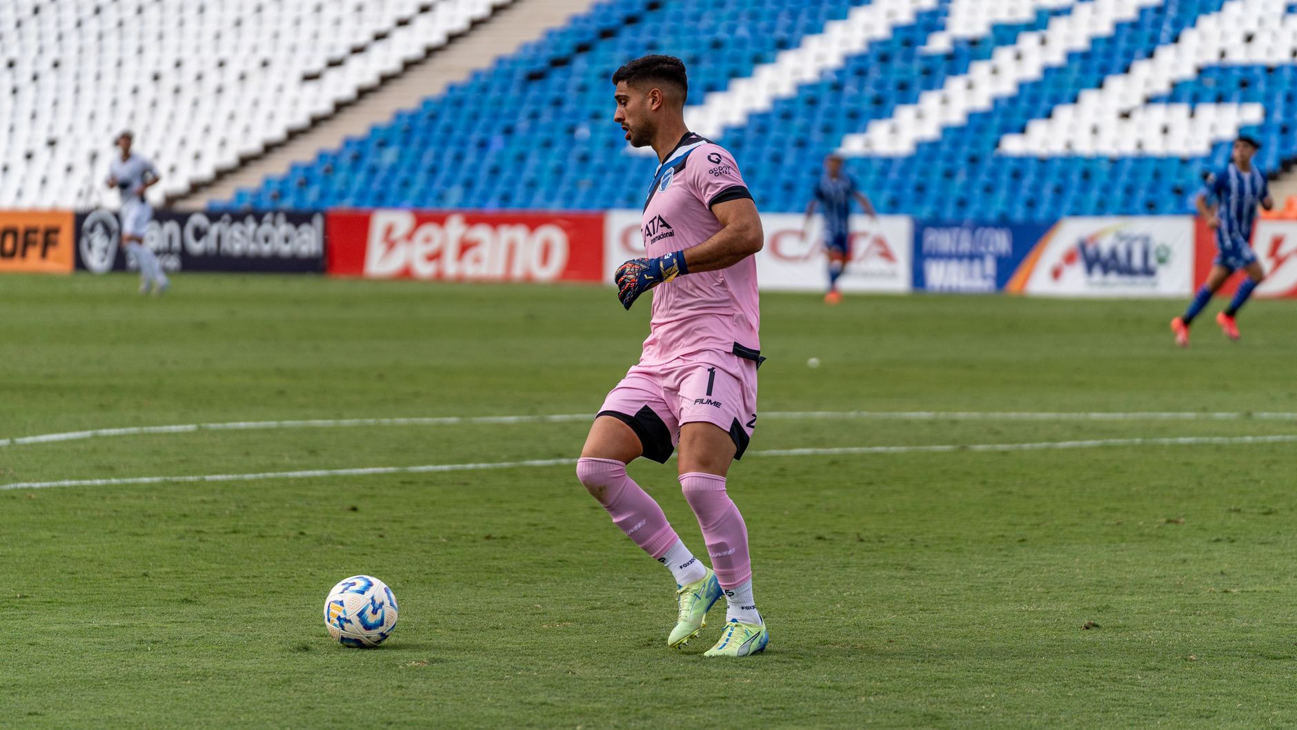 Goalkeeper in pink uniform kicking ball during competitive soccer match.