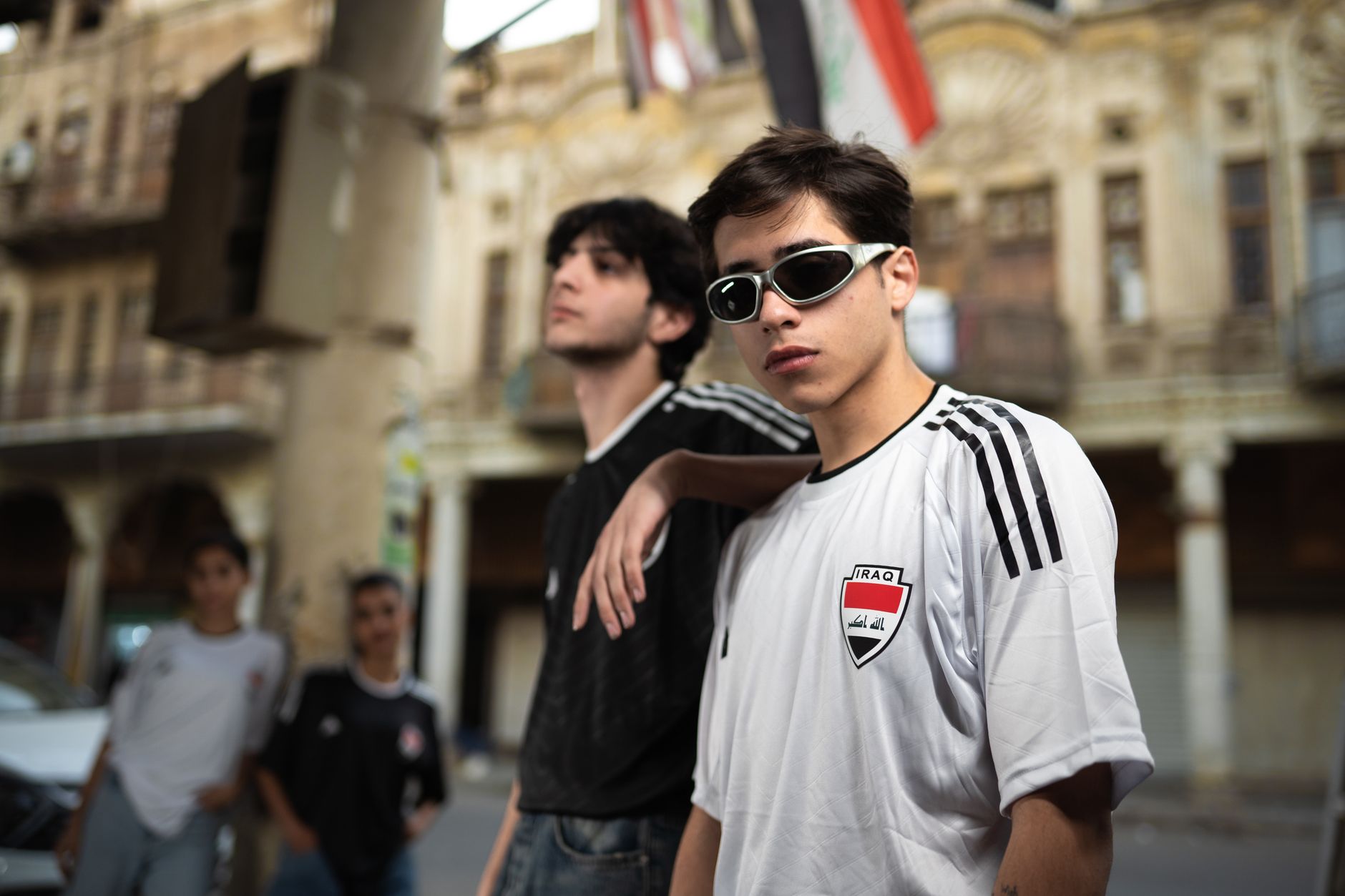 Young men wearing Iraq jerseys pose stylishly on a bustling street.