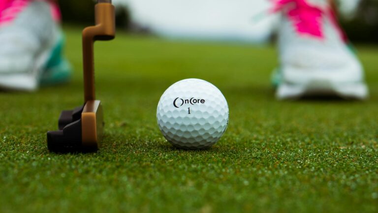 Golf ball and putter on green grass, ready for a putting shot.