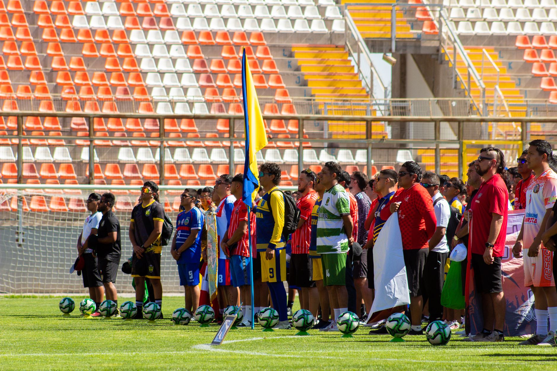 Multiple soccer teams stand in line in a brightly lit outdoor stadium for a ceremony or event.