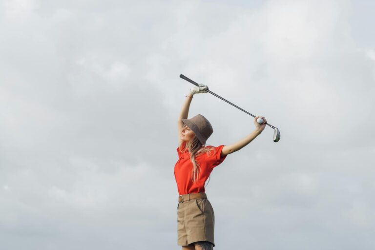 Woman in red shirt stretching with a golf club under cloudy skies, embracing an active lifestyle.