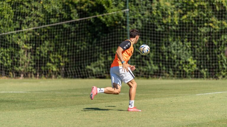 Adult male soccer player practicing skills on an outdoor field during a sunny day.