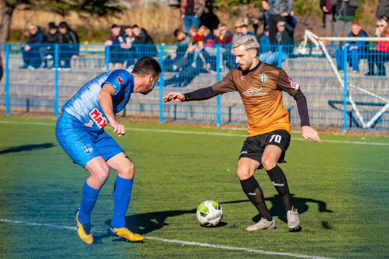 Two male soccer players in action during a competitive match on a grass field.