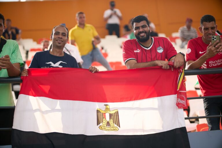 Cheerful Egyptian fans holding flag at a soccer match, enjoying the game.