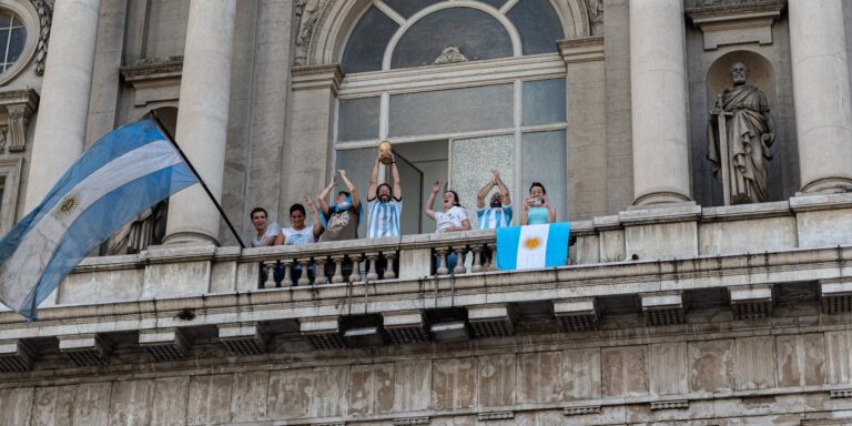 People celebrating with flags and a trophy on a Buenos Aires balcony.