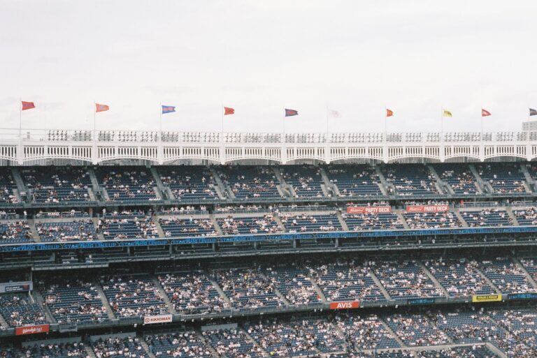 Crowd at Yankee Stadium watching a baseball game, flags waving atop tiers.