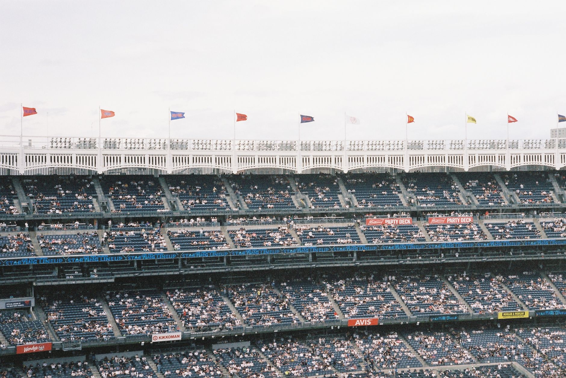 Crowd at Yankee Stadium watching a baseball game, flags waving atop tiers.