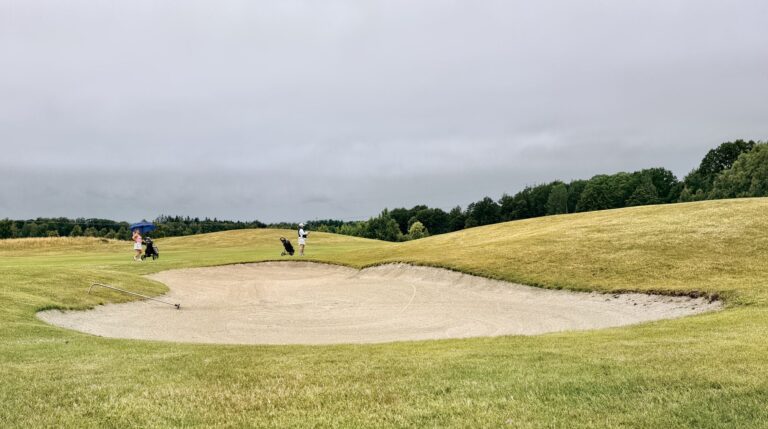 Two golfers on a lush golf course with a sand bunker in Skåne, Sweden.