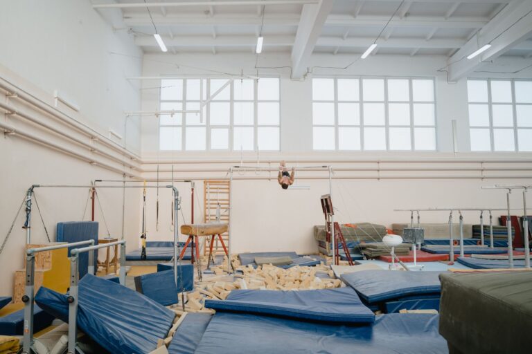 Bright indoor gymnastics facility with various equipment and an athlete training.