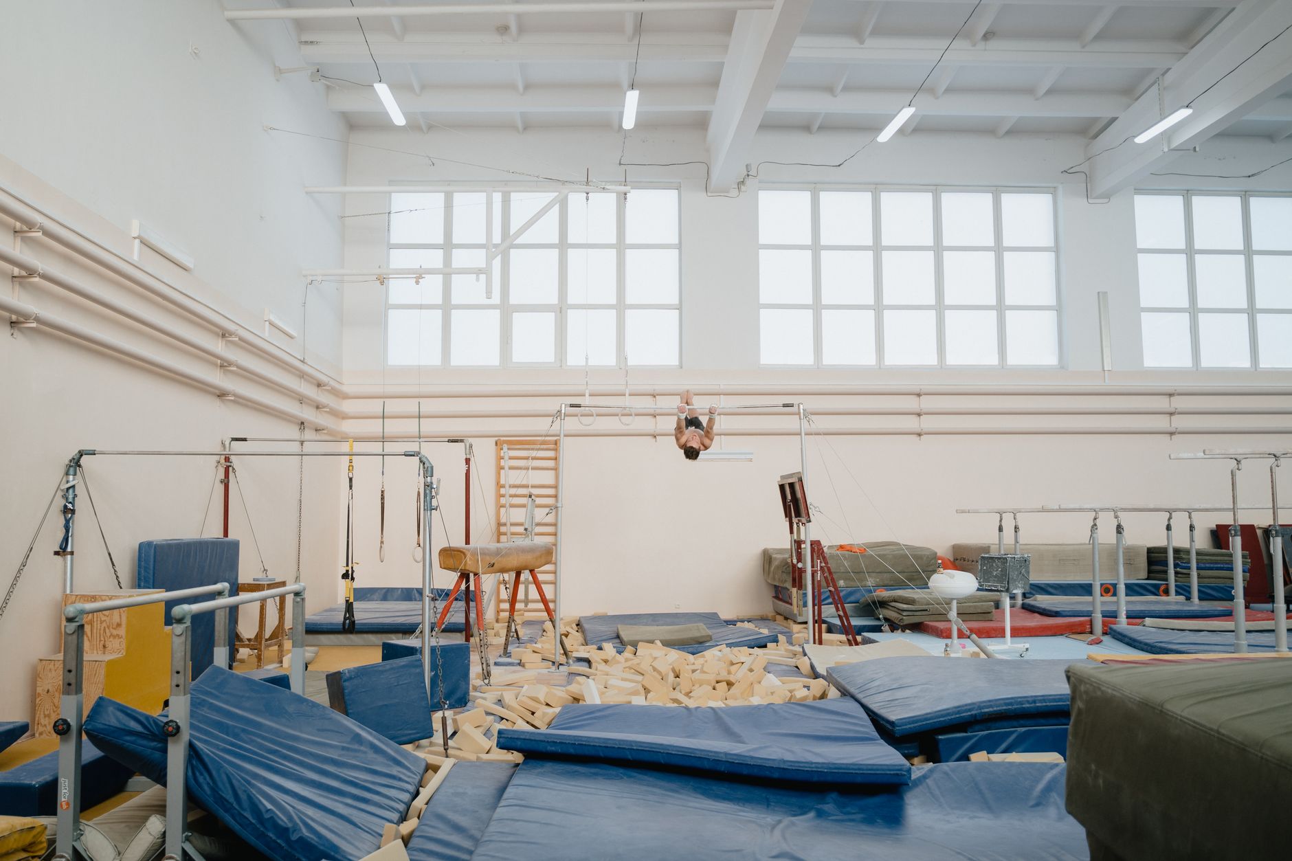 Bright indoor gymnastics facility with various equipment and an athlete training.