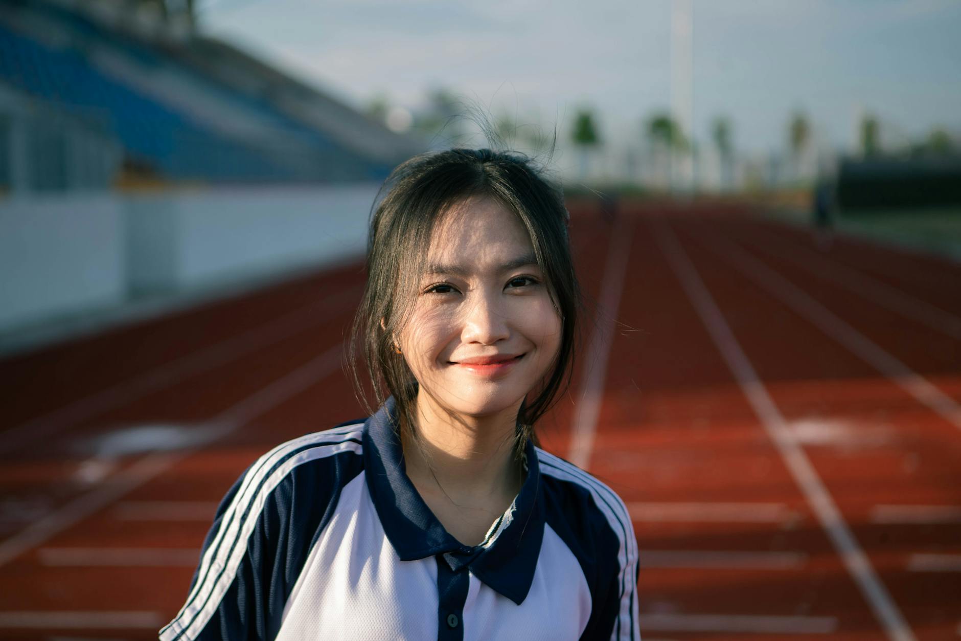 A young woman on an athletic track, smiling during daytime outdoor practice.