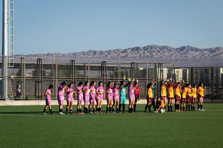Women's soccer teams lineup on outdoor field with mountain backdrop for match start.