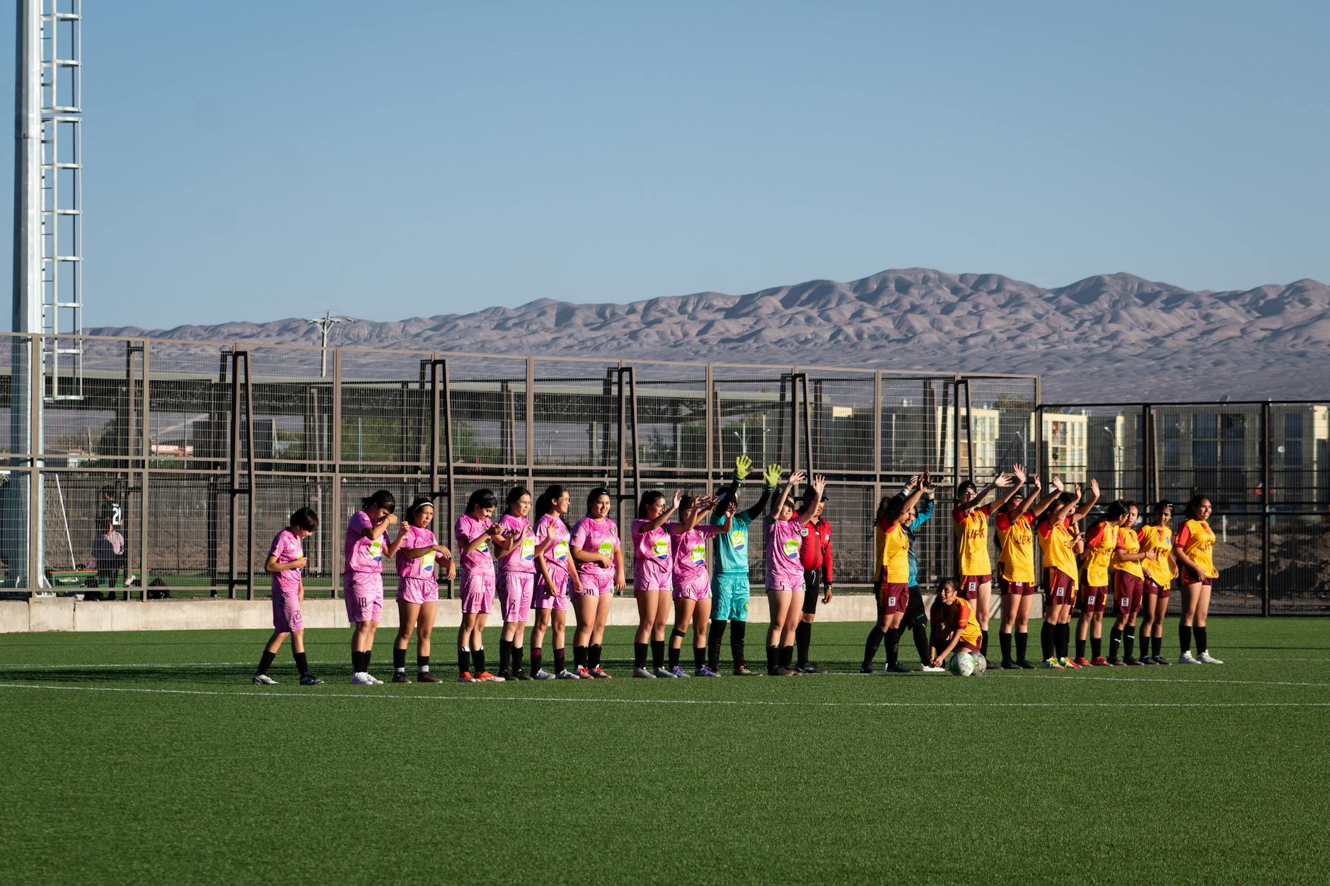 Women's soccer teams lineup on outdoor field with mountain backdrop for match start.