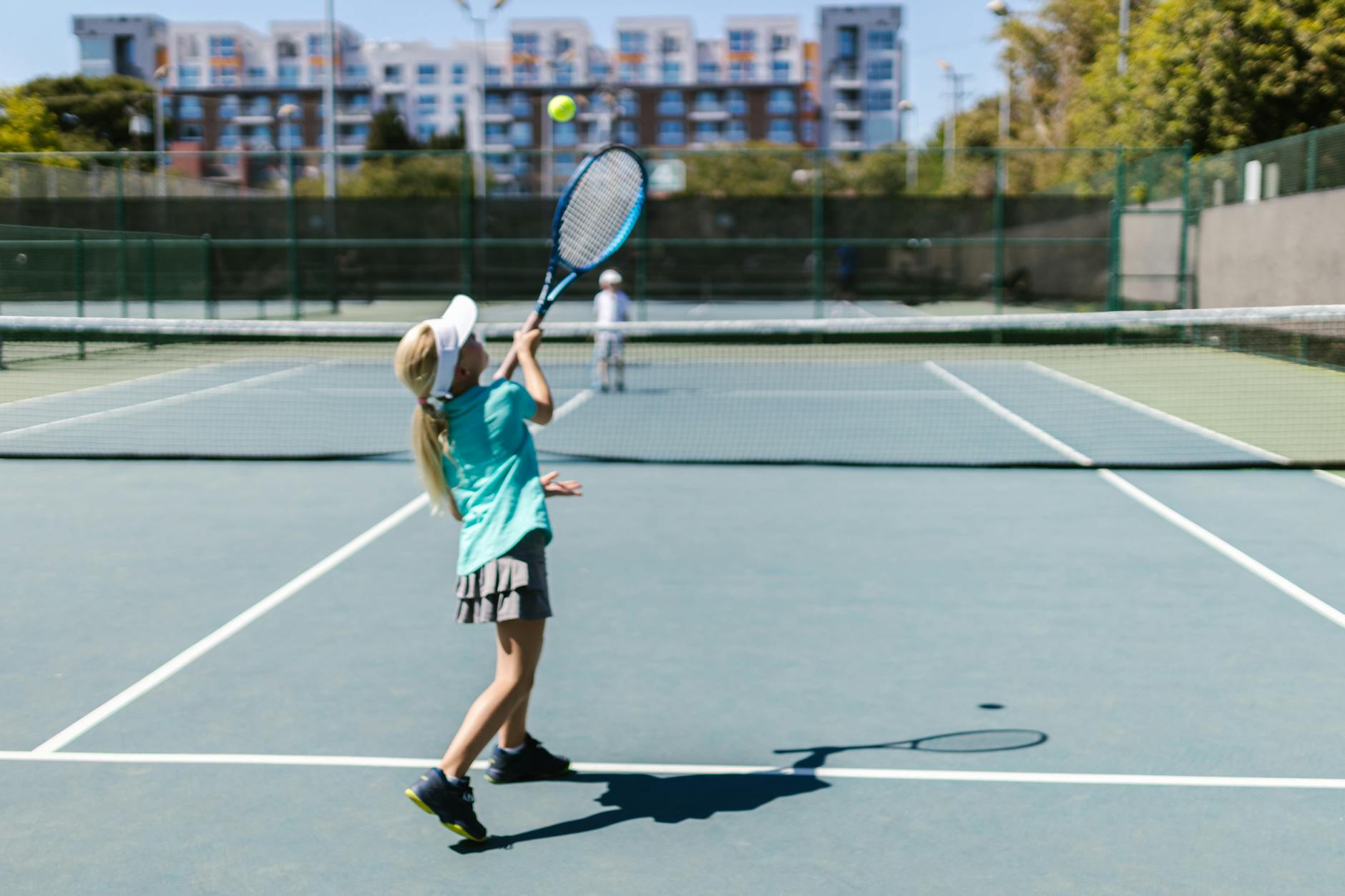 A girl in sportswear hitting a tennis ball on a sunny outdoor court.
