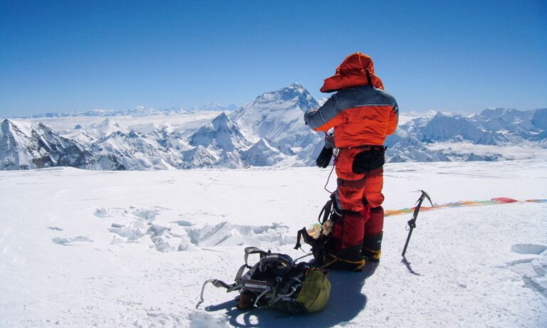 Mountaineer in puffer jacket on snowy peak in Nepal's Himalayas.