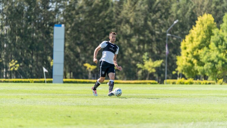 Soccer player dribbling a ball on a sunny outdoor field with lush greenery.